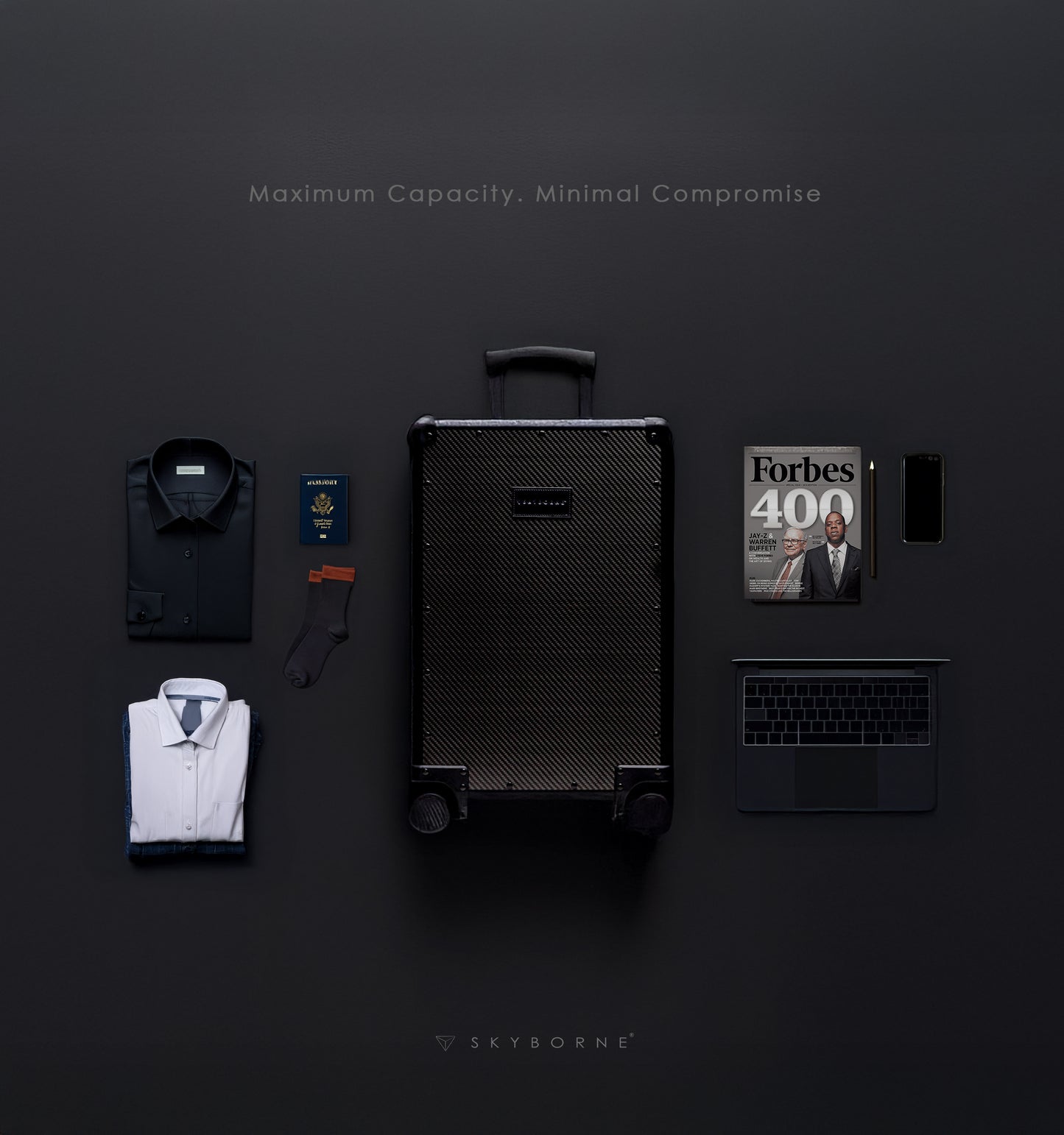 Black suitcase with shirts, a laptop, and a magazine on a dark background